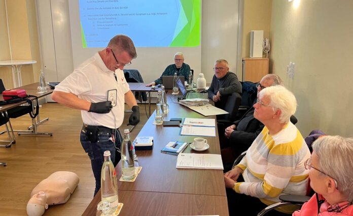 Rettungsassistent Michael Kluge-Dummer (li.) demonstrierte dem Seniorenbeirat die Handhabung und die Funktionsweise von automatisierten externen Defibrillatoren (AEDs) und erklärte, dass grüne Schilder mit einem weißen Herzsymbol in der Mitte auf freizugängliche Laien-Defibrillatoren hinweisen. (Foto: Astrid Zens / DRK-Kreisverband Ahrweiler e.V.)